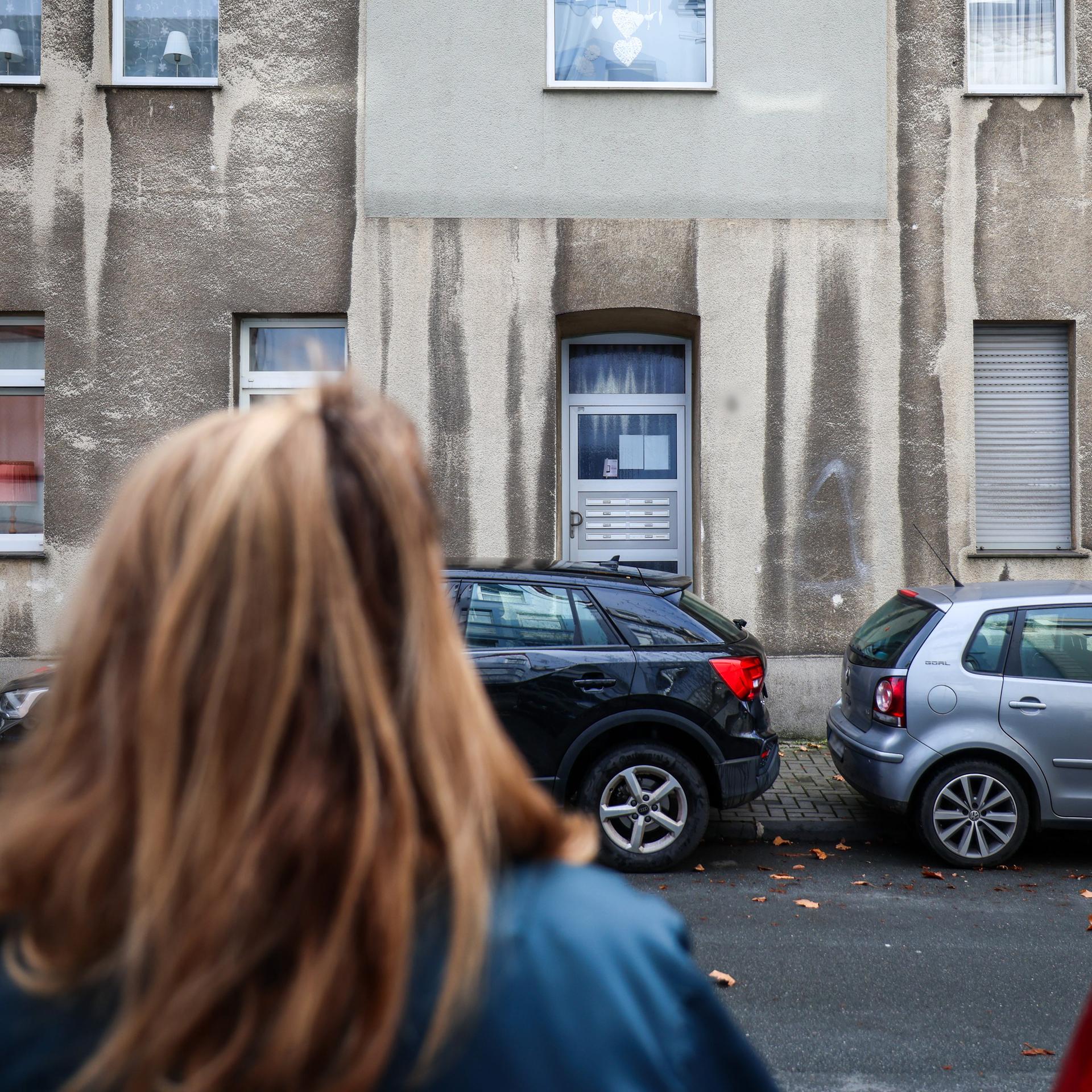 Eine Frau steht vor einem Mehrfamilienhaus.