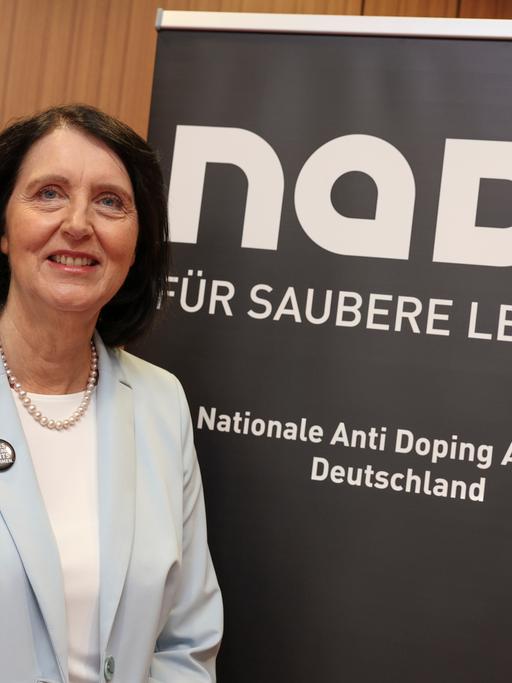 Andrea Gotzmann steht vor einem Plakat der Nationalen Anti Doping Agentur. Unter dem Schriftzug NADA steht "Für saubere Leistung".