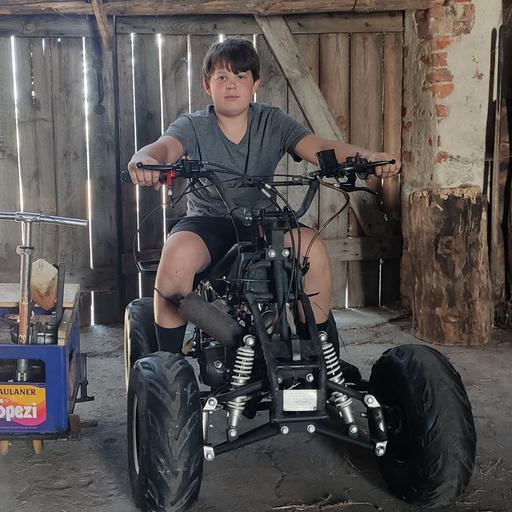 Ein Junge sitzt auf einem Quad. Daneben steht das von ihm aus einer Getränkekiste und einem Roller gebaute Gefährt.