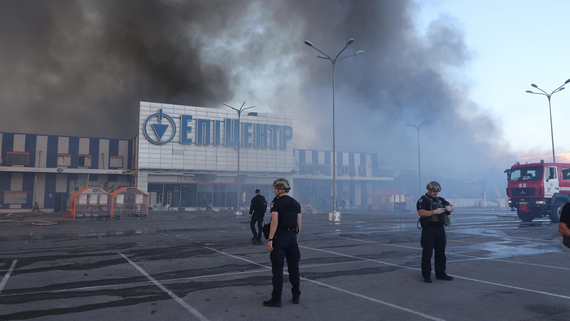 Beamte stehen vor einem brennenden Supermarkt in Charkiw.