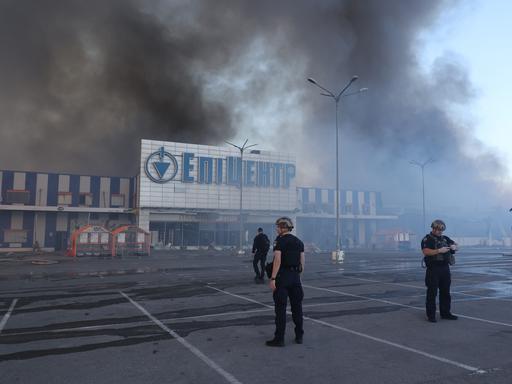 Beamte stehen vor einem brennenden Supermarkt in Charkiw.