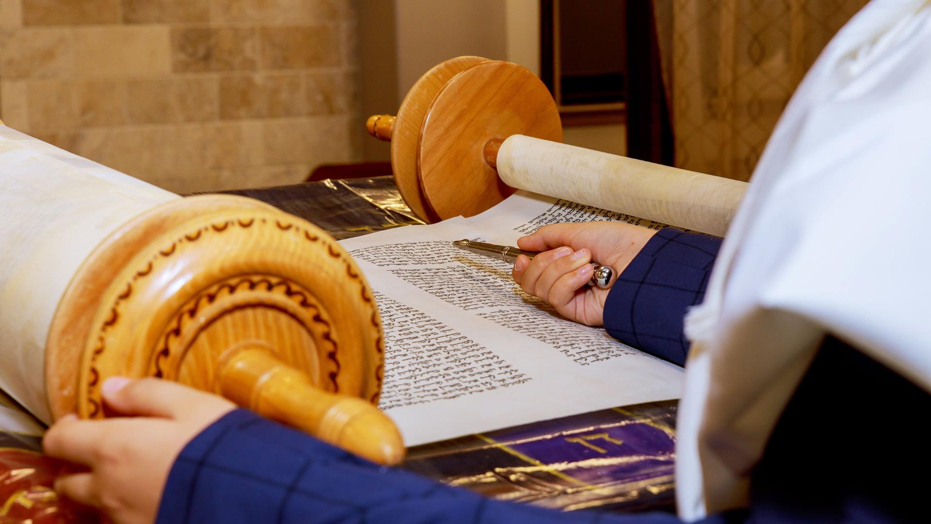Ein Junge hält einen silbernen Stab, eine Lesehilfe, in der Hand und liest aus der Tora-Schriftrolle.