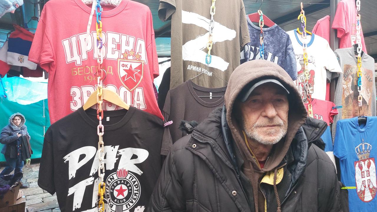 Ein Mann an seinem Marktstand mit vielen T-Shirts, eins darunter mit einem Z als Aufdruck.