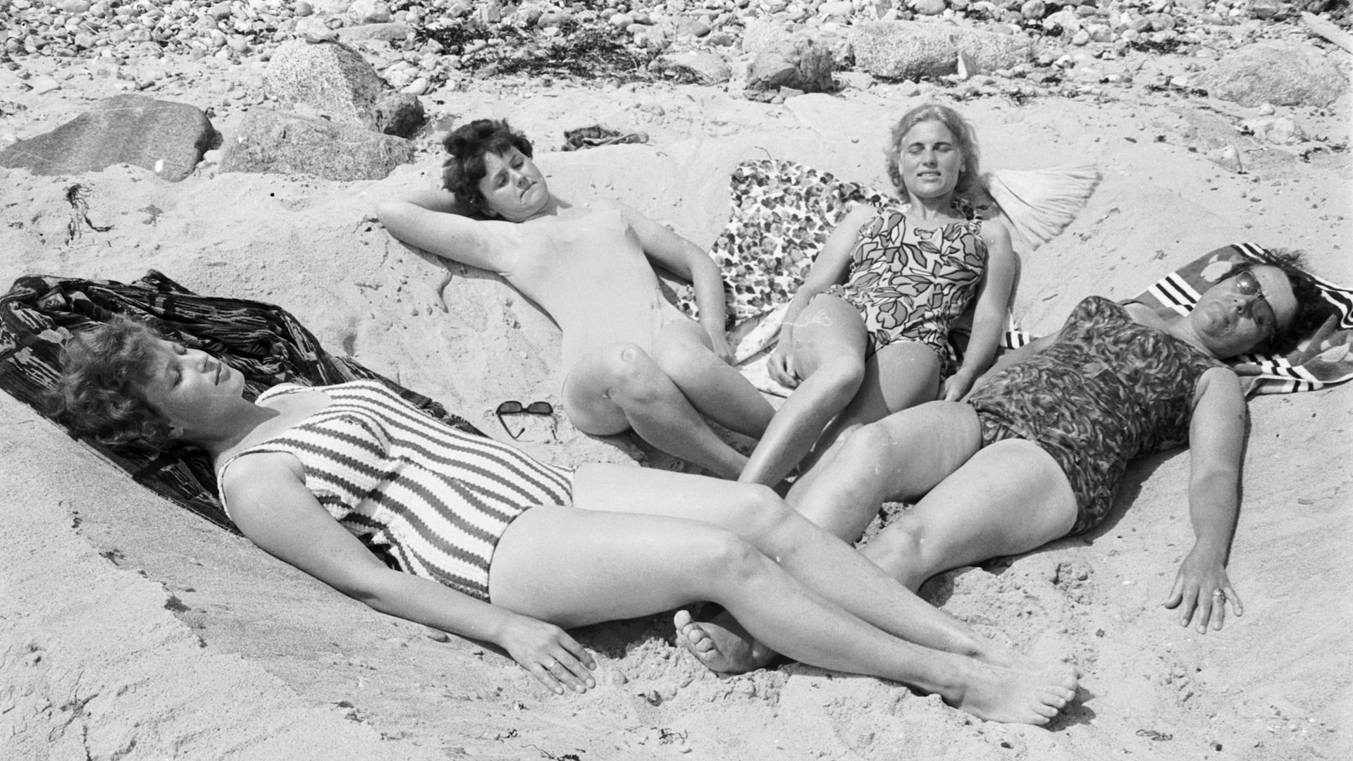 Historisches Schwarzweißfoto von vier Frauen aus den 1950er Jahren, die in Badekleidung an einem Strand liegen.