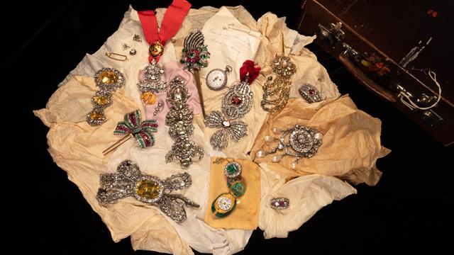 Schmuckstücke liegen auf beigen Tüchern vor schwarzem Hinter-Grund. 