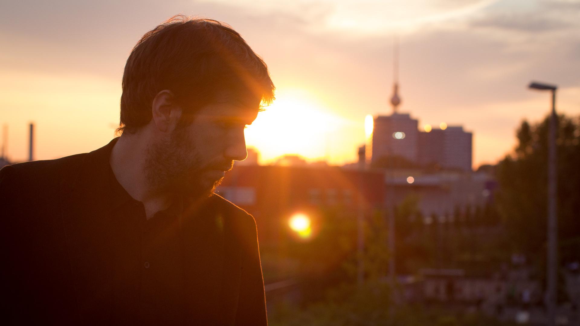 Antoine Villoutreix steht im Abendlicht seitlich zur Kamera gewandt, hinter ihm taucht die Berliner Stadtkulisse mit dem Fernsehturm auf.