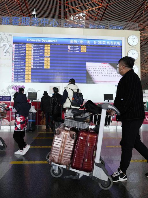 Menschen mit Gepäck an einem Flughafen in Peking.