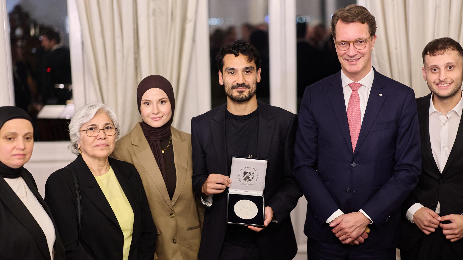 Hendrik Wüst (CDU, 2.v.r), Ministerpräsident von Nordrhein-Westfalen, steht mit Ilkay Gündoğan (3.v.r), ehemaliger Kapitän der Deutschen Fußballnationalmannschaft, und Mitgliedern der Familie Genç in der Sommerresidenz der Deutschen Botschafterin. Gündogan hält die Mevlüde-Genç-Medaille in der Hand. 