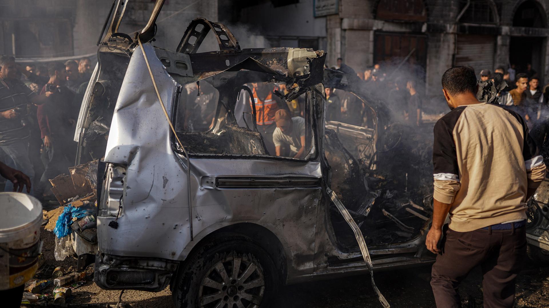 Bei israelischen Luftangriffen im Gazastreifen sind mehrere Menschen getötet worden. Viele Menschen stehen in Gaza-Stadt um ein ausgebranntes Auto herum. 