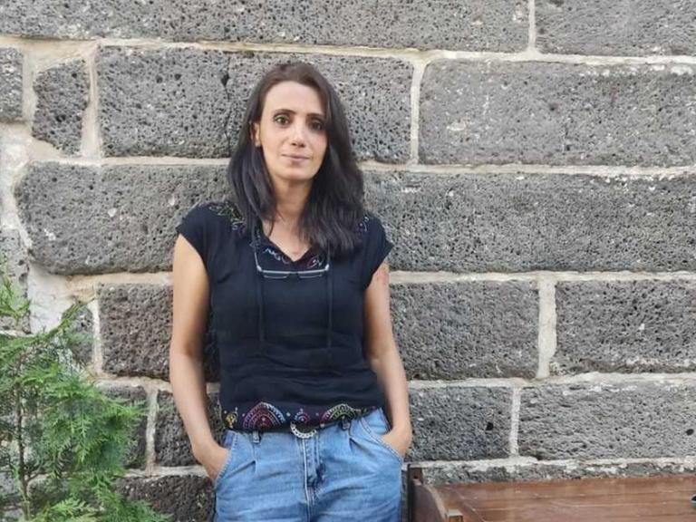 Meral Şimşek steht in lockerer Pose vor einer Steinmauer.