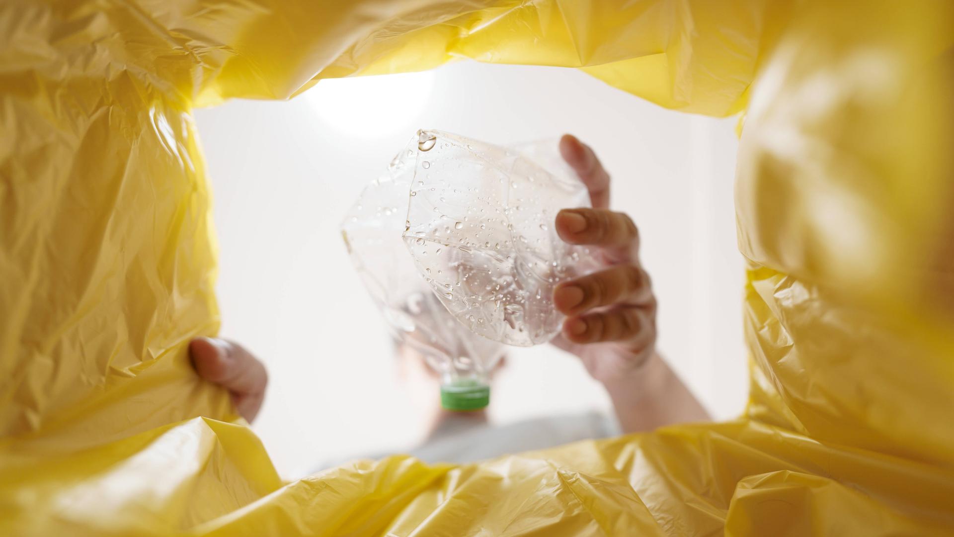 Ein Mann wirft eine Plastikflasche in einen Müllbeutel. 