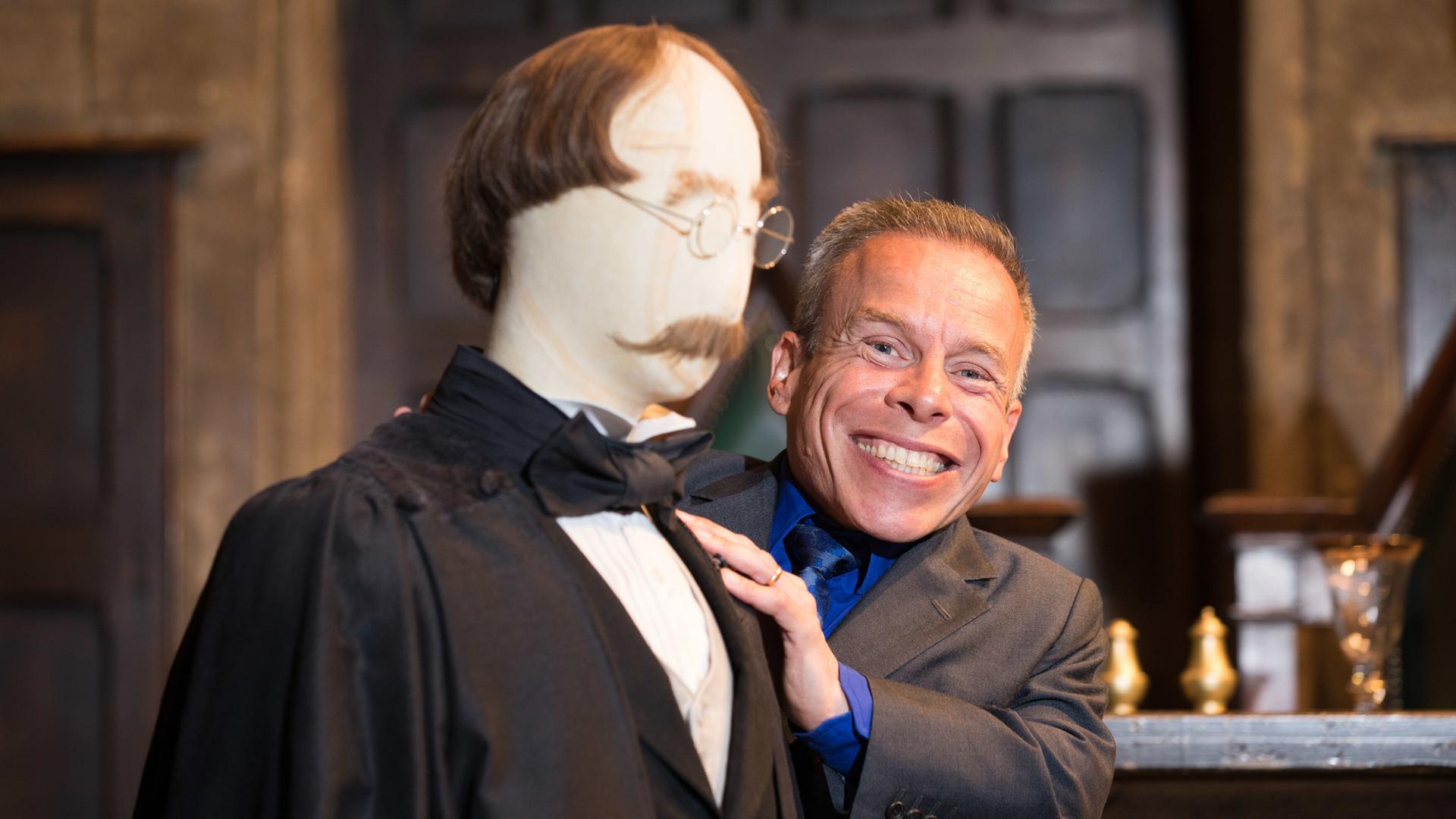 Der britische Schauspieler Warwick Davis neben seinem Originalkostüm von der Figur Professor Flitwick in der Warner Bros. Studio Tour London