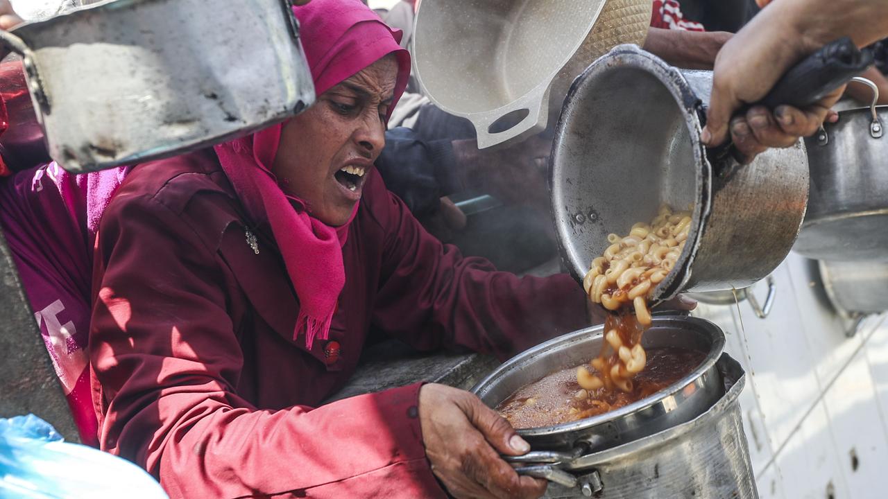 Eine Frau mit verzweifeltem Gesichtsausdruck bekommt Essen in ihren Topf gefüllt. Um sie herum drängen sich Menschen mit leeren Töpfen.