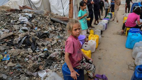 Am Rande eines Trümmerfeldes warten Kinder in Gaza mit bunten Plastikkanistern auf die Ausgabe von frischem Trinkwasser.