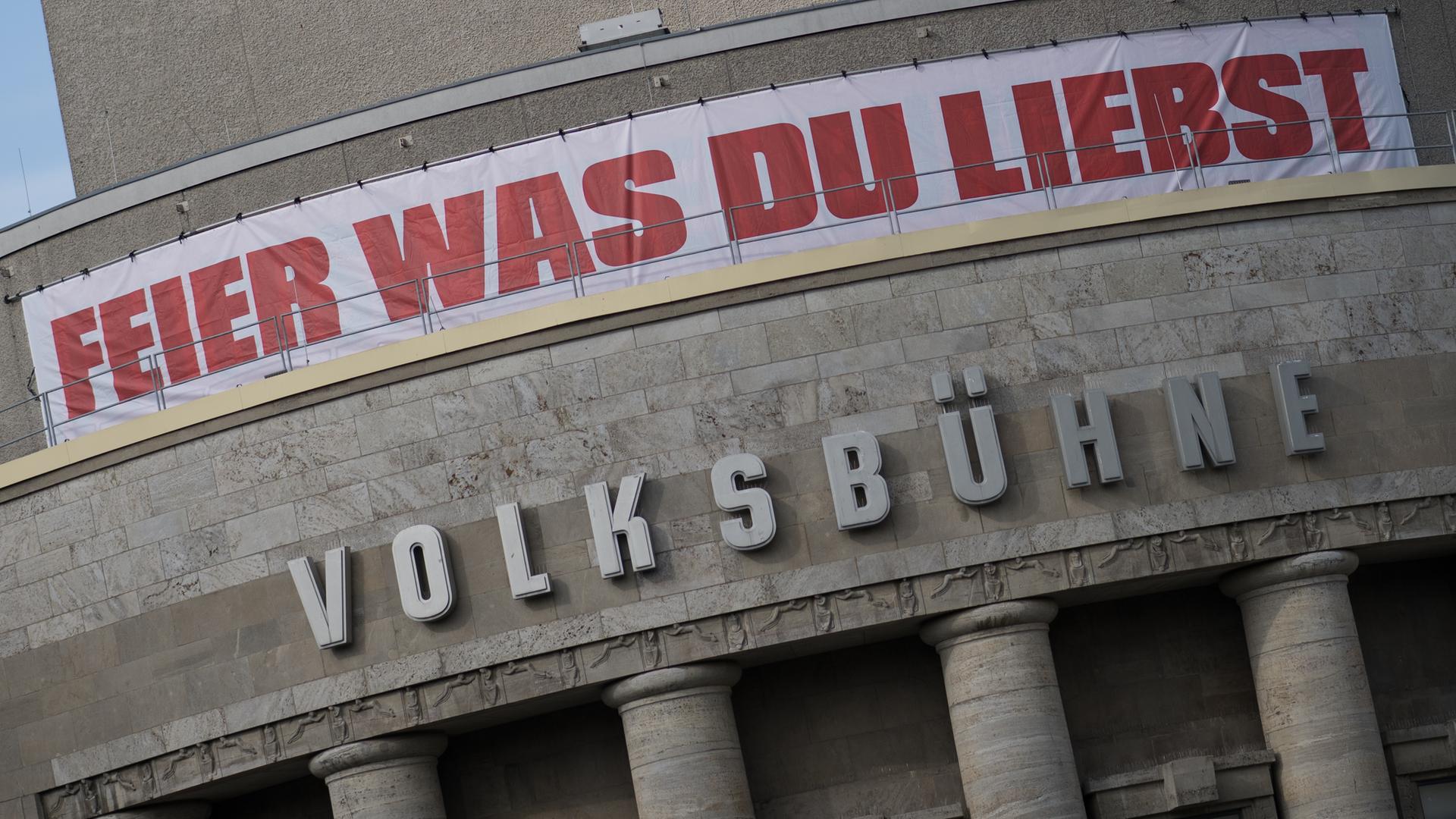 Die Fassade der Berliner Volksbühne mit einem weißen Banner mit der roten Aufschrift "Feier was Du liebst"