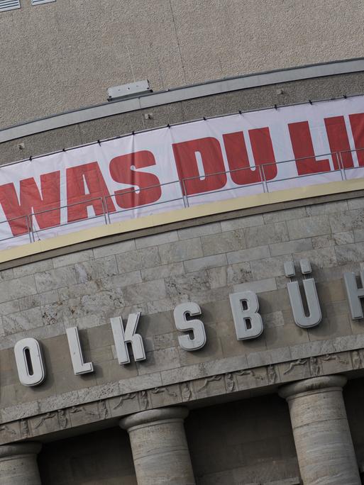 Die Fassade der Berliner Volksbühne mit einem weißen Banner mit der roten Aufschrift "Feier was Du liebst"