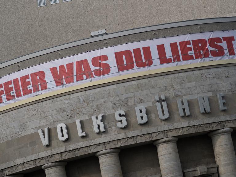 Die Fassade der Berliner Volksbühne mit einem weißen Banner mit der roten Aufschrift "Feier was Du liebst"