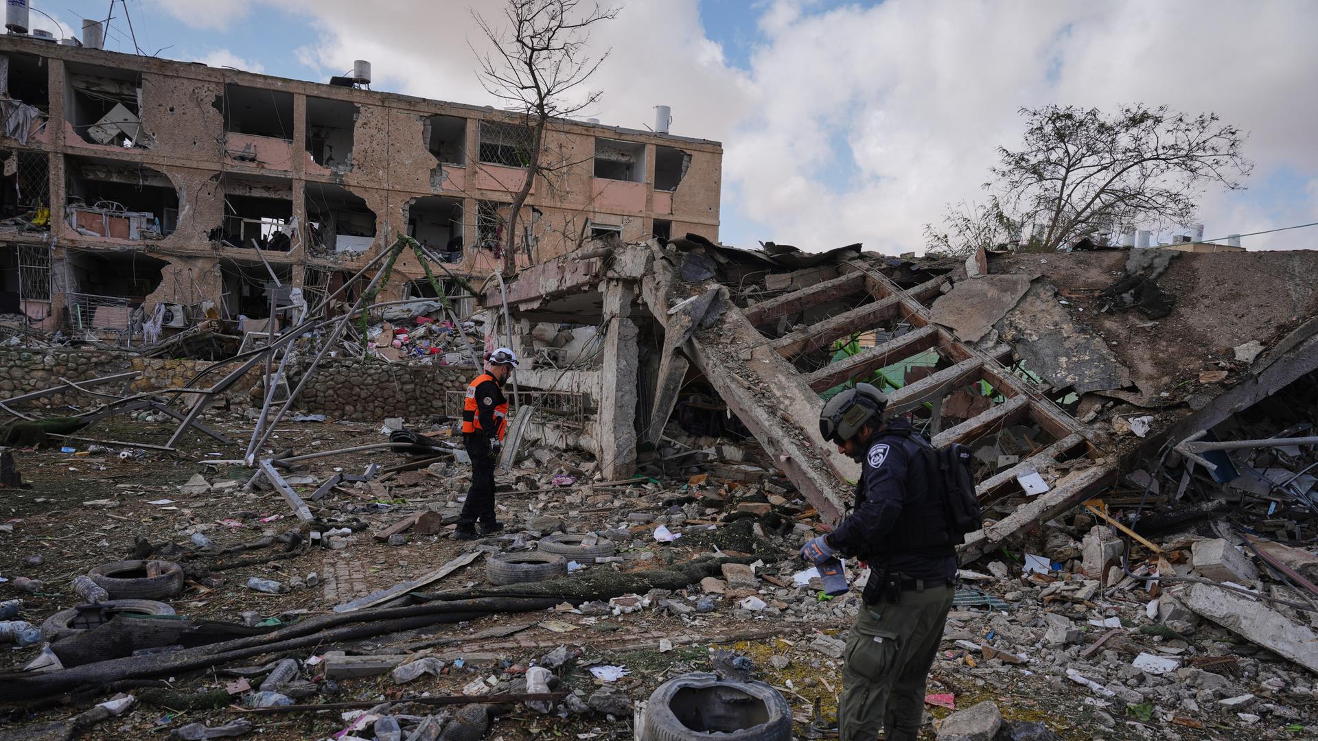 Auf einem Trümmerfeld vor einem zerstörten Haus in Dimona stehen zwei Rettungskräfte.