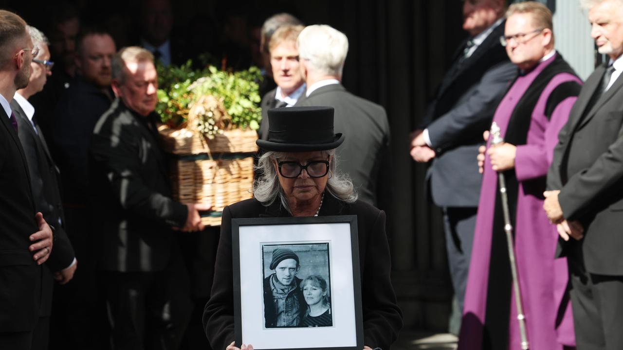 Ein Bild von Glen Hansard wird von einer Frau vor dem Sarg getragen, als dieser nach seiner Beerdigung die St. Patrick’s Cathedral in Dublin verlässt.
      