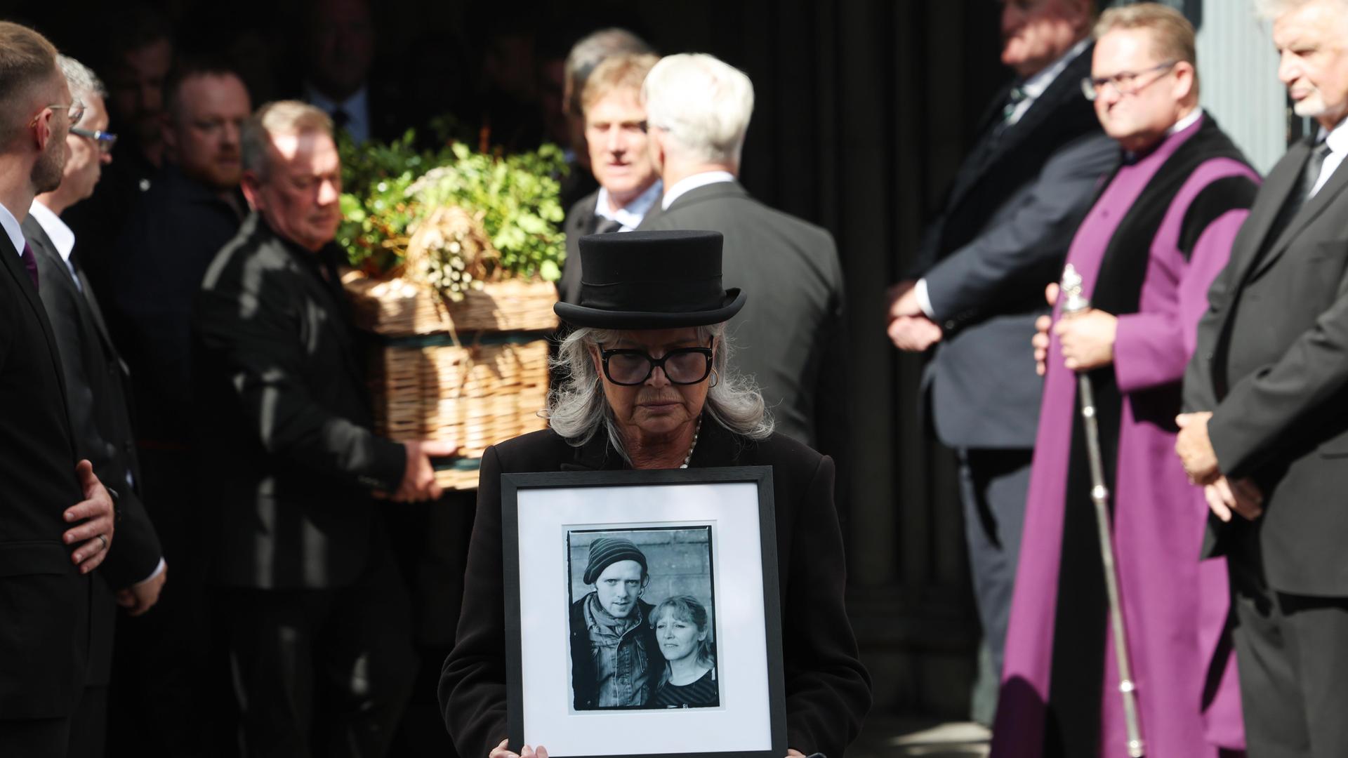 Ein Bild von Glen Hansard wird von einer Frau vor dem Sarg getragen, als dieser nach seiner Beerdigung die St. Patrick’s Cathedral in Dublin verlässt.
Ein Bild von Glen Hansard wird von einer Frau vor dem Sarg getragen, als dieser nach seiner Beerdigung die St. Patrick’s Cathedral in Dublin verlässt.