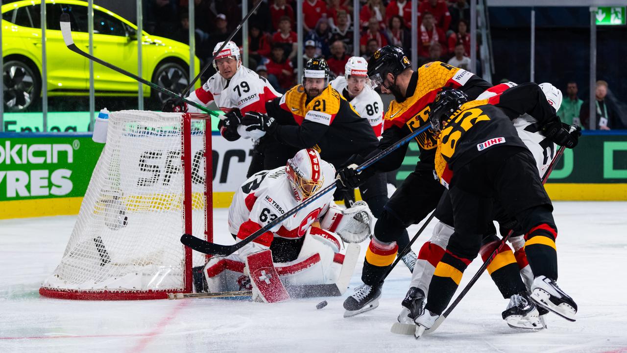 Das Bild zeigt eine Szene aus dem Eishockey-Spiel: Die deutschen Spieler in Schwarz und Gold greifen an, die Schweizer Spieler in Weiß und Rot verteidigen.