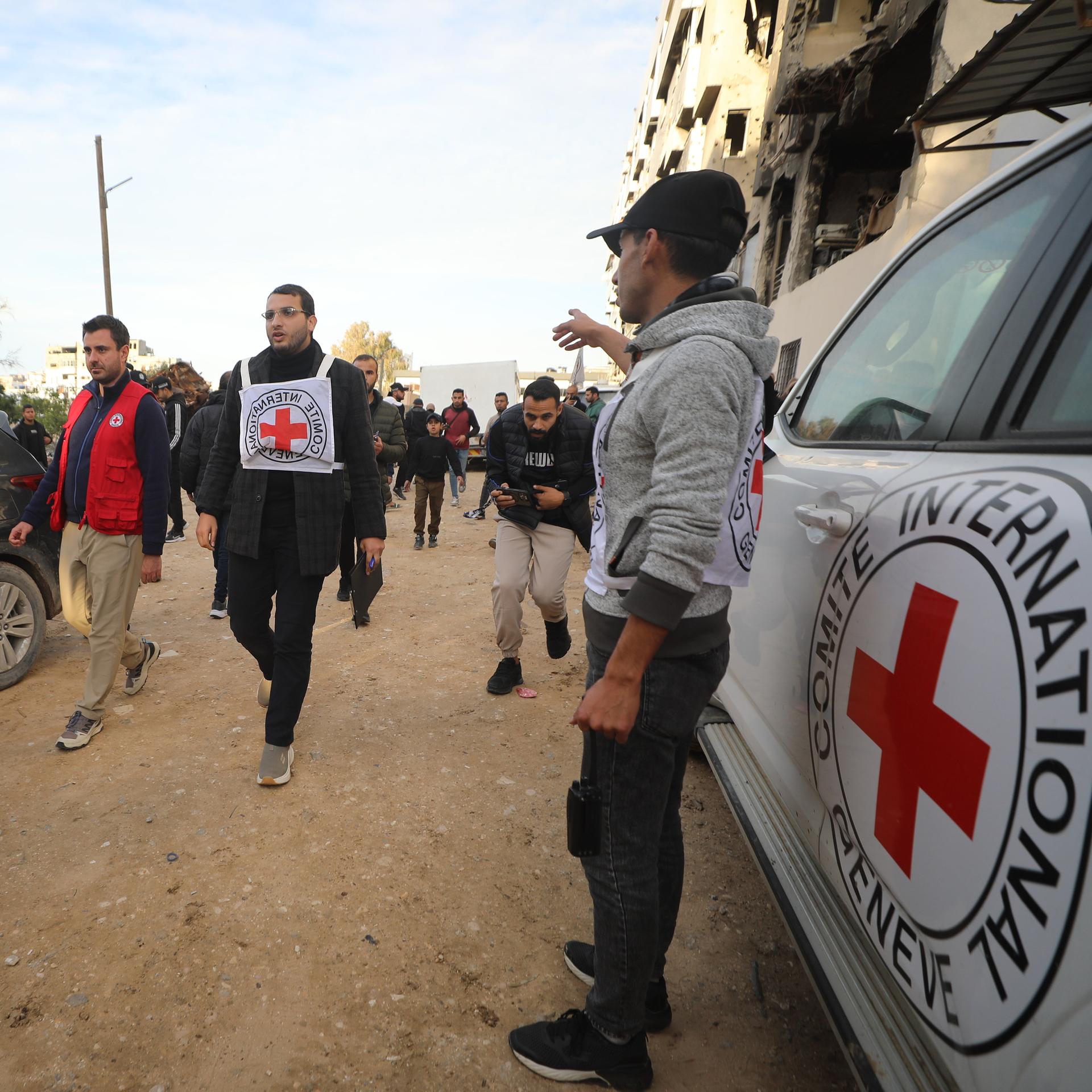 Mehrere Männer laufen über eine Straße, begleitet von Autos mit den Logos des Roten Kreuzes.