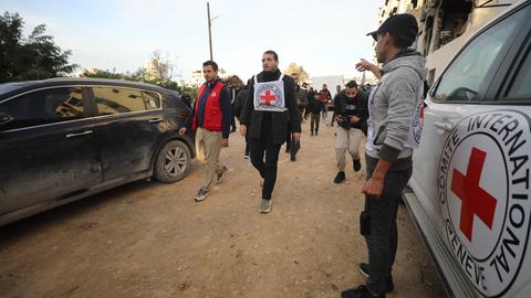 Mehrere Männer laufen über eine Straße, begleitet von Autos mit den Logos des Roten Kreuzes.