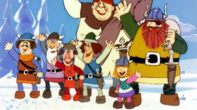 Im Still aus "Wickie und die starken Männer" steht der kleine Wickie neben sechs großen Männern. Alle tragen Wikingerkleidung und winken.