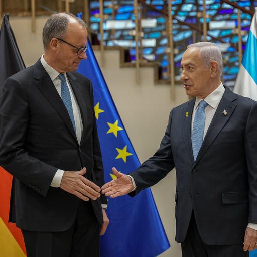Bundeskanzler Friedrich Merz und der israelische Regierungschef Benjamin Netanjahu stehen vor den Flaggen Deutschlands, der EU und Israels und reichen sich die Hand.