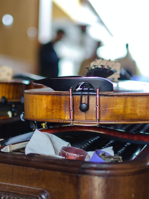 Zwei Geigen im Vordergrund liegen auf einem Tisch, dahinter erscheinen schemenhaft die Musiker.
