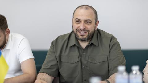 Der ukrainische Verteidigungsminister Rustem Umerow sitzt an einem Tisch und lächelt. 