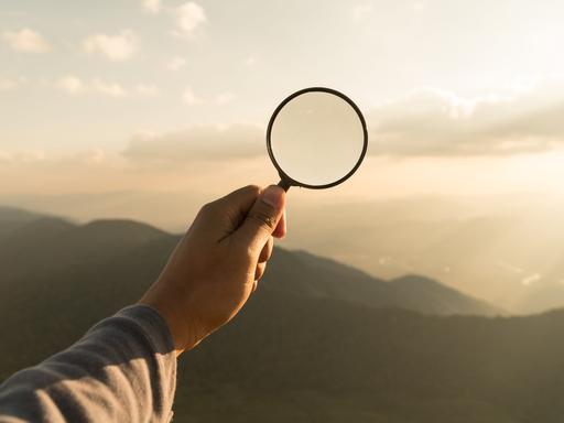 Eine Lupe wird von einer Hand gehalten.