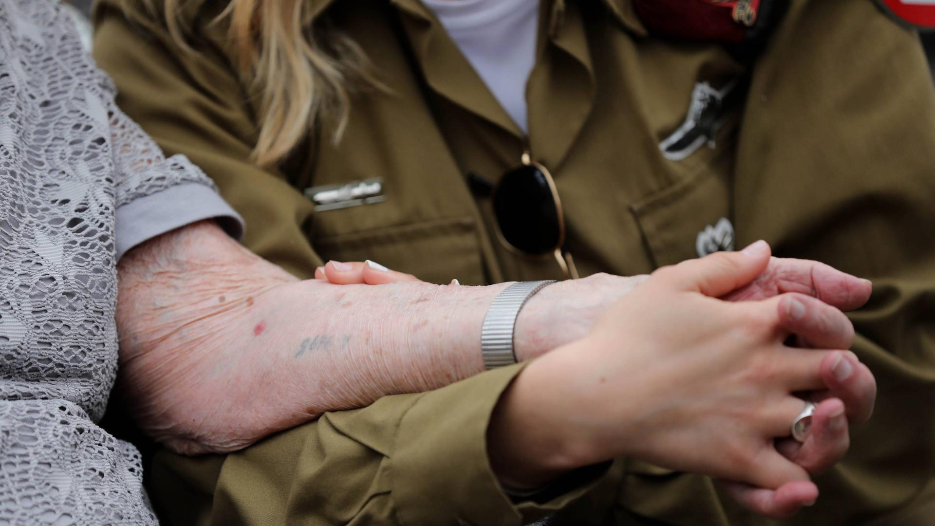 Holocaust-Überlebende Hanna Tessler mit ihrer Enkelin Shira Tessler. Eine israelische Soldatin hält die Hand ihrer Großmutter, die den Holocaust überlebt hat. Auf den Arm hat sie eine tätowierte Nummer. 