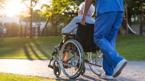 Rückansicht eines männlichen Pflegers mit einer älteren Patientin im Rollstuhl. 
