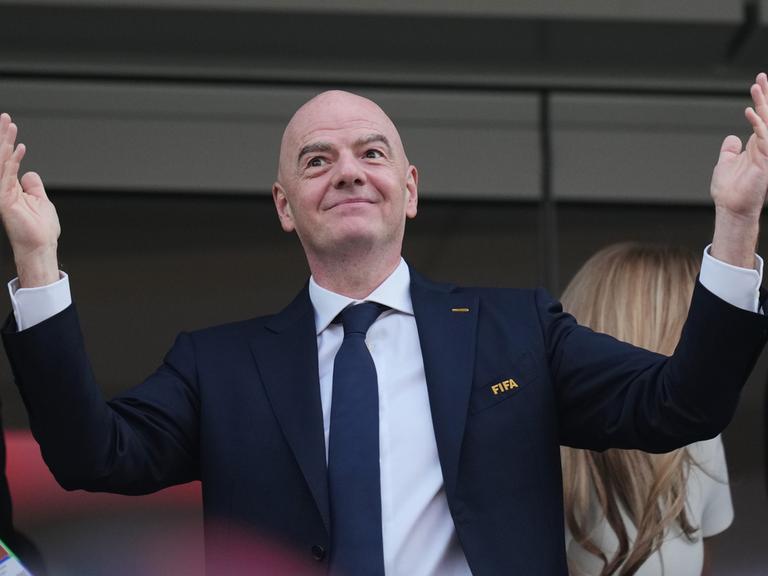 FIFA-Präsident Gianni Infantino hat die Arme ausgebreitet und hält dabei die Hände nach oben. Er trägt einen dunkelblauen Anzug.