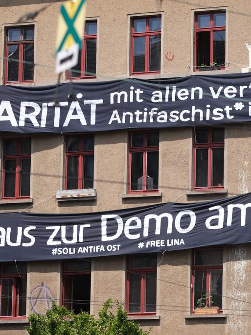 Transparente mit der Aufschrift "Solidarität mit allen verfolgten Antifaschist*innen!" und "Heraus zur Demo am Tag X" hängen an der Fassade eines Hauses.