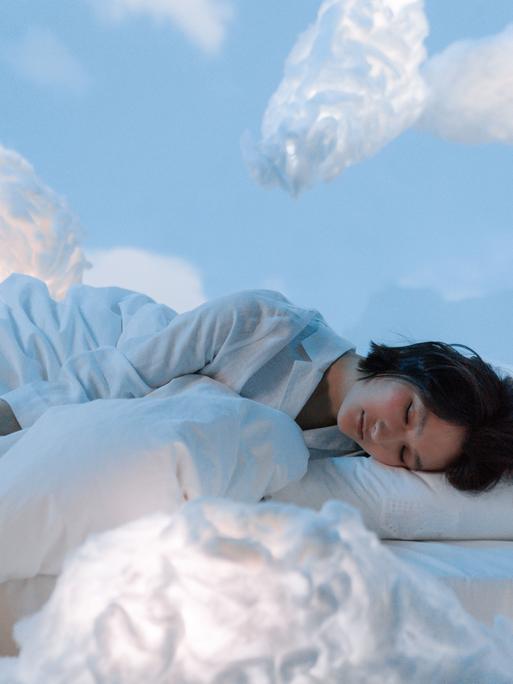 Eine Frau liegt schlafend in einem Bett aus Wolken.