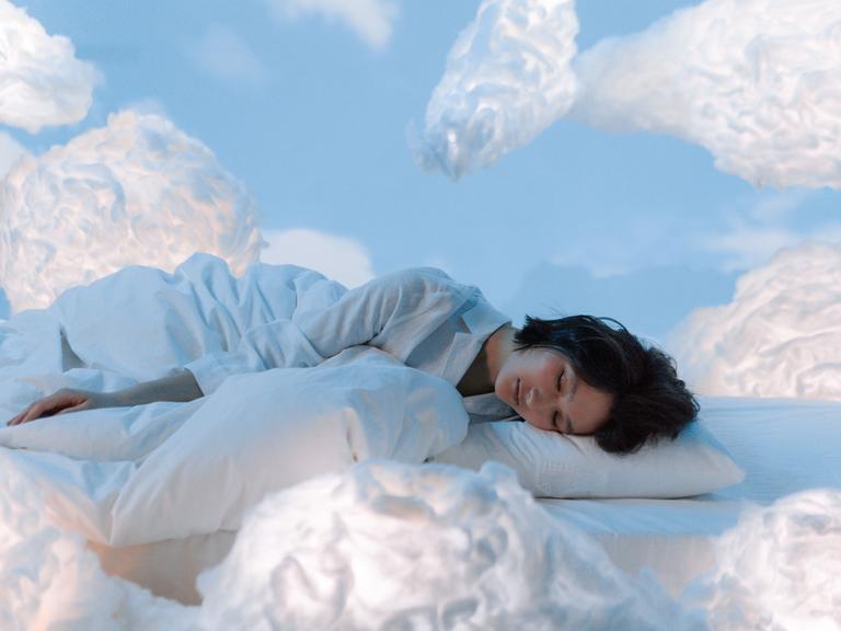 Eine Frau liegt schlafend in einem Bett aus Wolken.