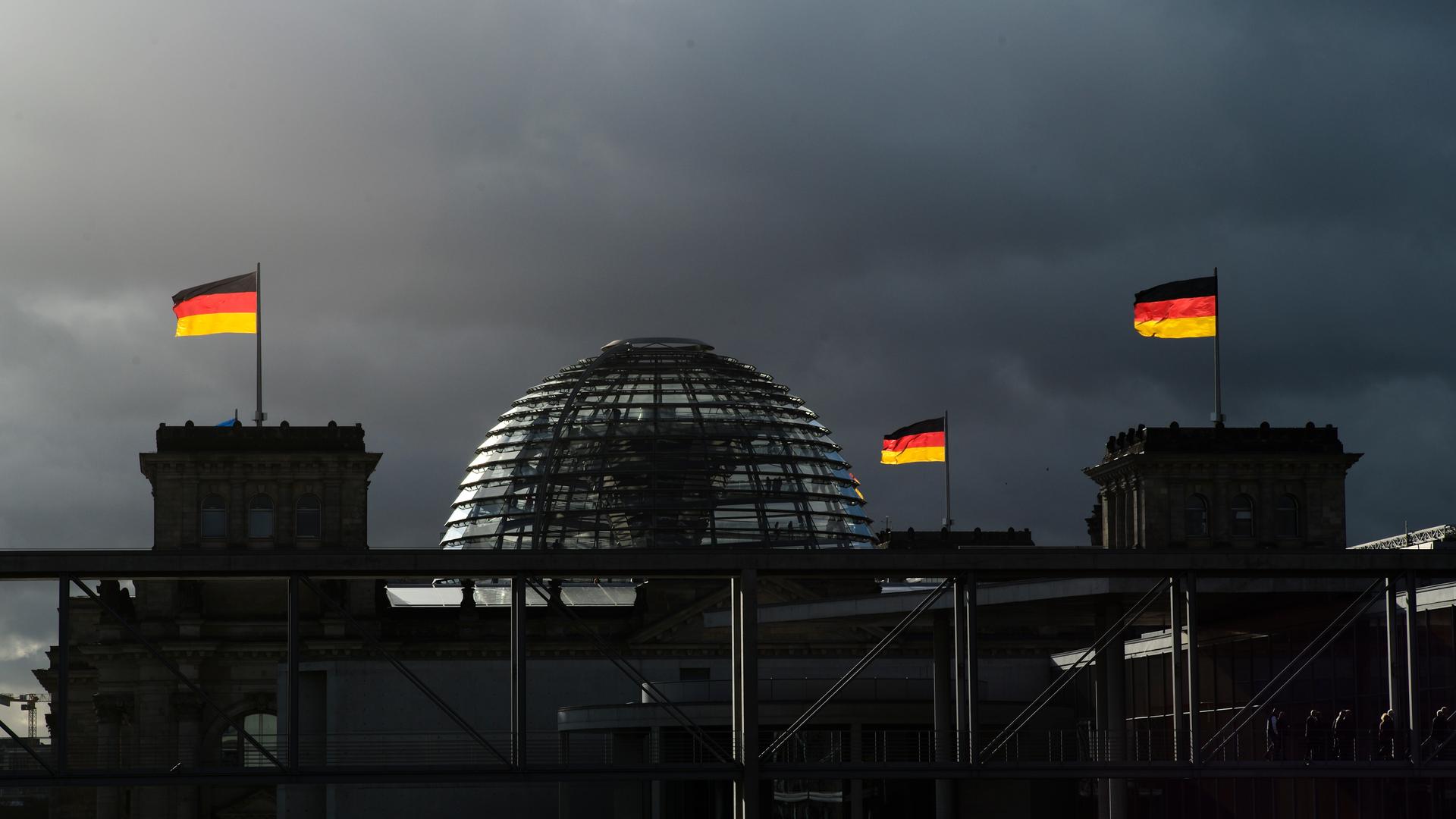 Deutsche Nationalflaggen leuchten auf dem Reichstagsgebäude in Berlin vor dunklen Wolken.