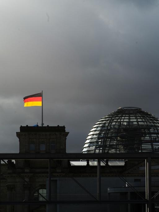 Deutsche Nationalflaggen leuchten auf dem Reichstagsgebäude in Berlin vor dunklen Wolken.