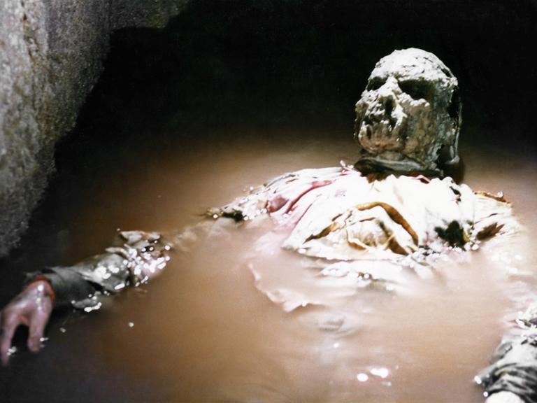 Ein Zombie liegt in dreckigem Wasser. Still aus "Über dem Jenseits" von Lucio Fulci.  © Fulvia Films