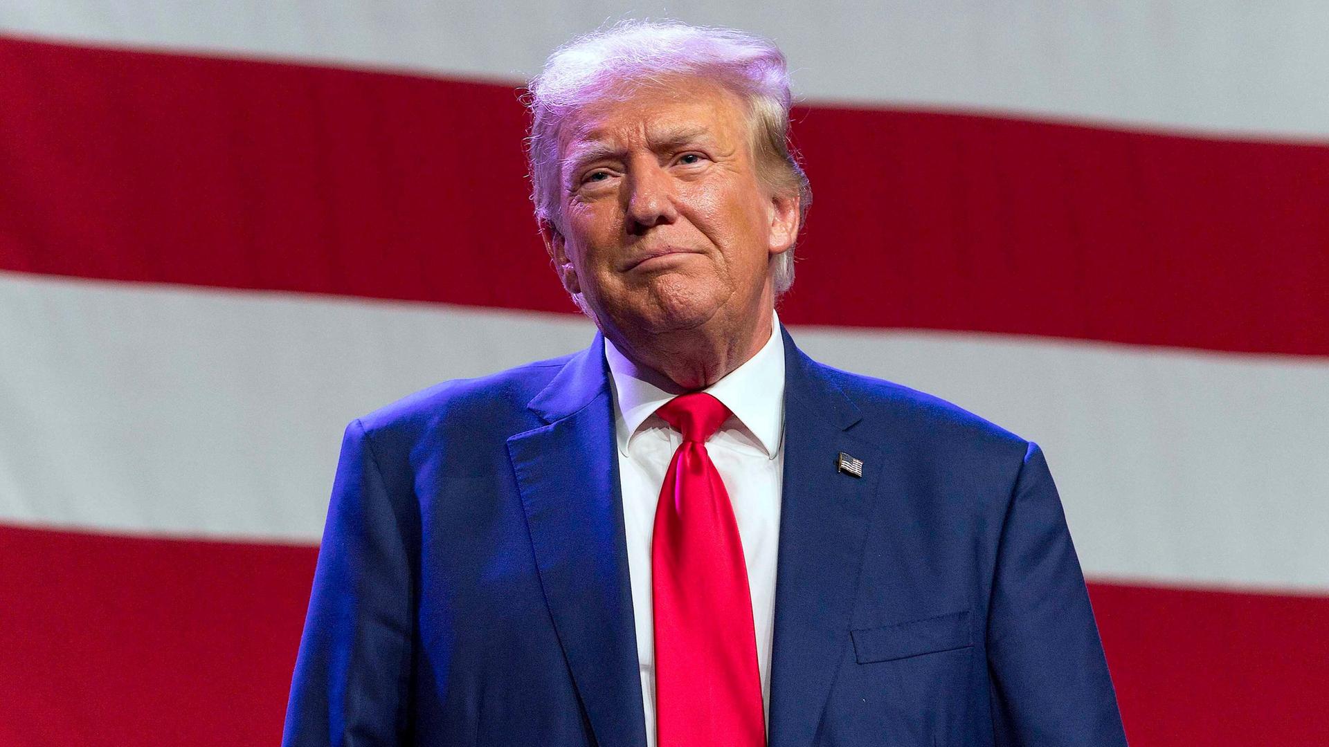 Der ehemalige US-Präsident Donald Trump steht von einer US-Flagge.