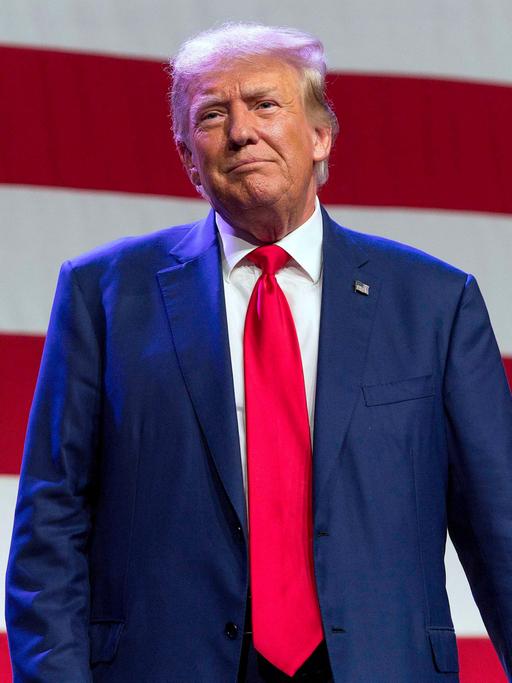 Der ehemalige US-Präsident Donald Trump steht von einer US-Flagge.