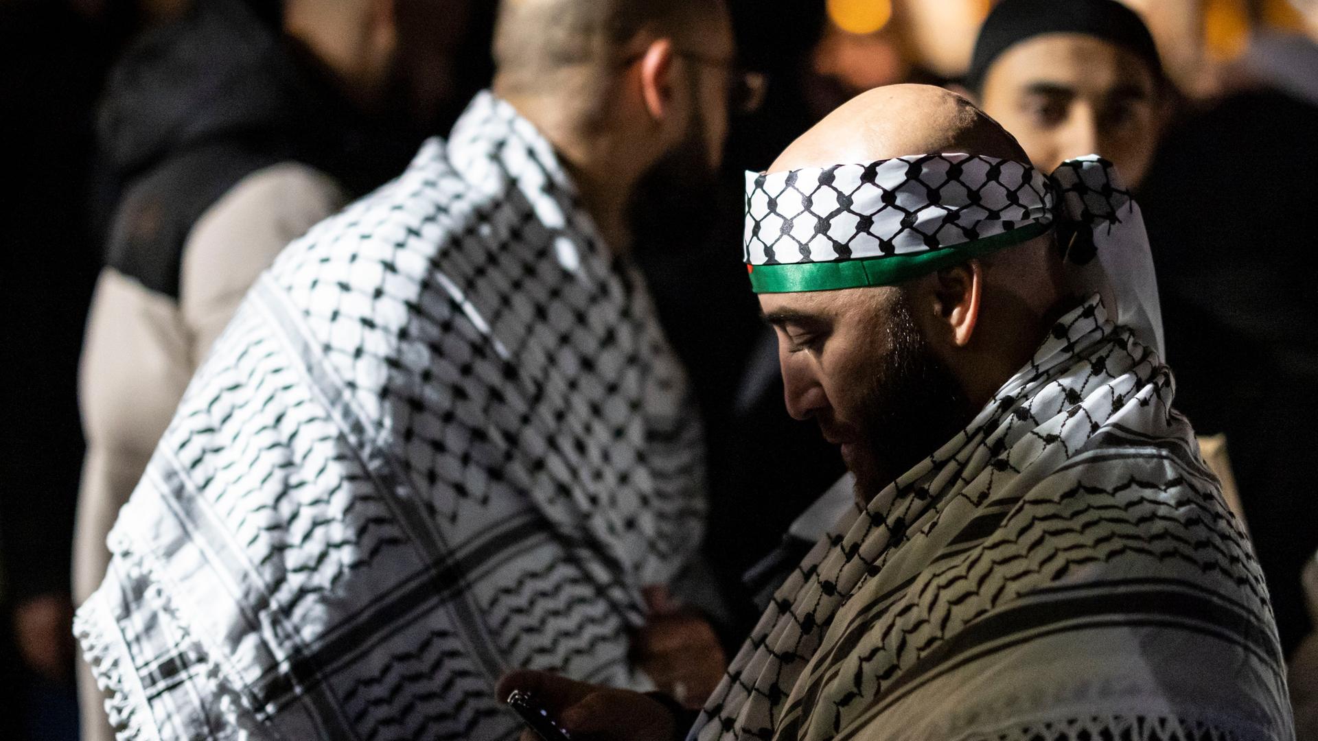 Im Zentrum des Bildes ein Teilnehmer mit palästinensischen Tüchern bei einer Kundgebung, um ihn herum weitere Männer mit palästinensischen Tüchern