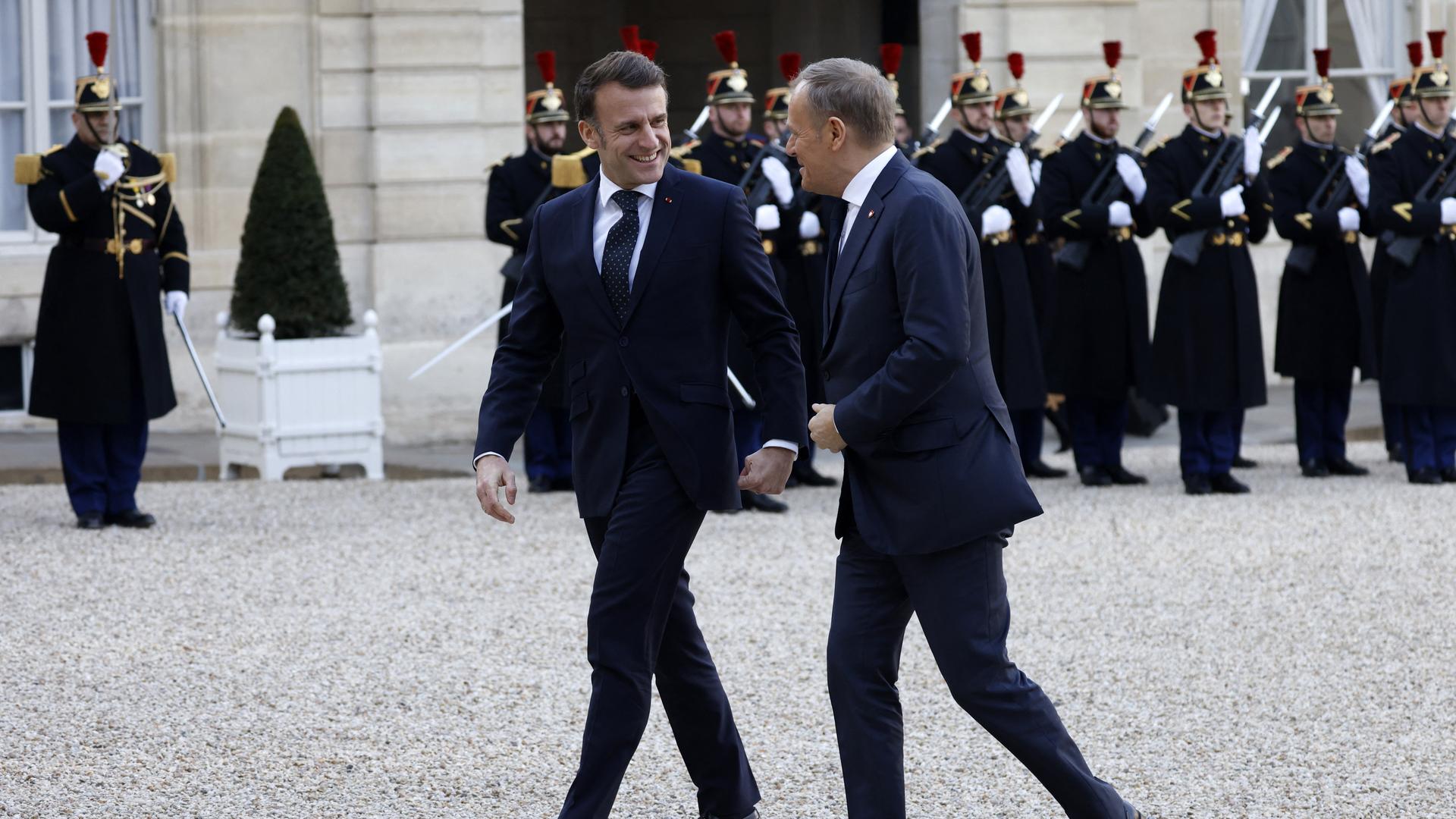 Frankreichs Emmanuel Macron geht mit Polens Premier Donald Tusk über den Vorplatz des Elysée-Palastes. Die beiden lächeln sich zu. Im Hintergrund stehen uniformierte Sicherheitskräfte.