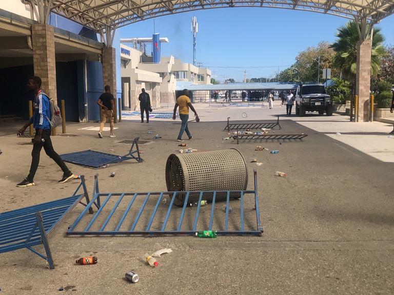 Auf einer Straße in Haitis Hauptstadt Port-au-Prince liegen umgestürzte Absperrgitter und ein Mülleimer. Vereinzelte Männer laufen in verschiedene Richtungen.