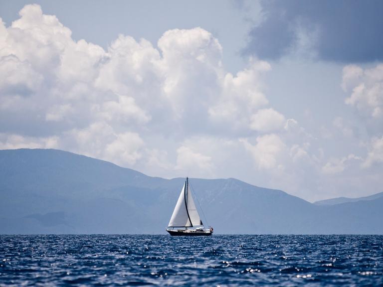 Segelboot auf See vor Bergen und Himmel.