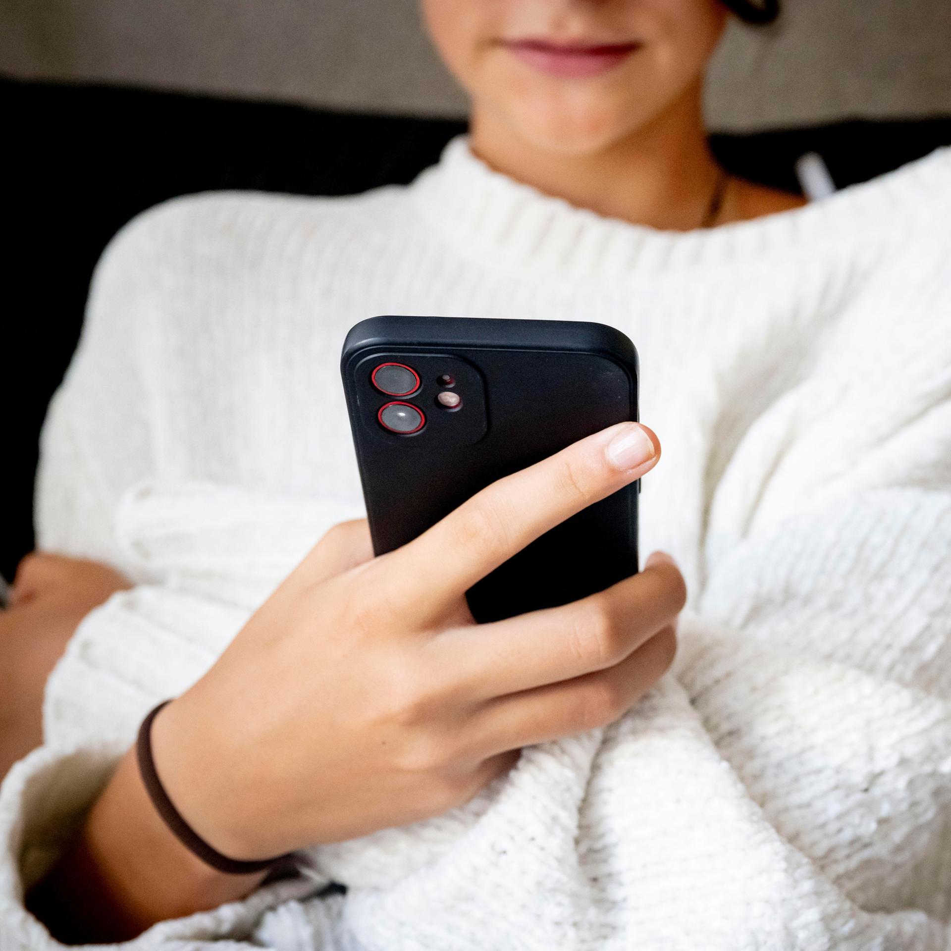 Eine junge Frau hält ein Handy in der Hand.