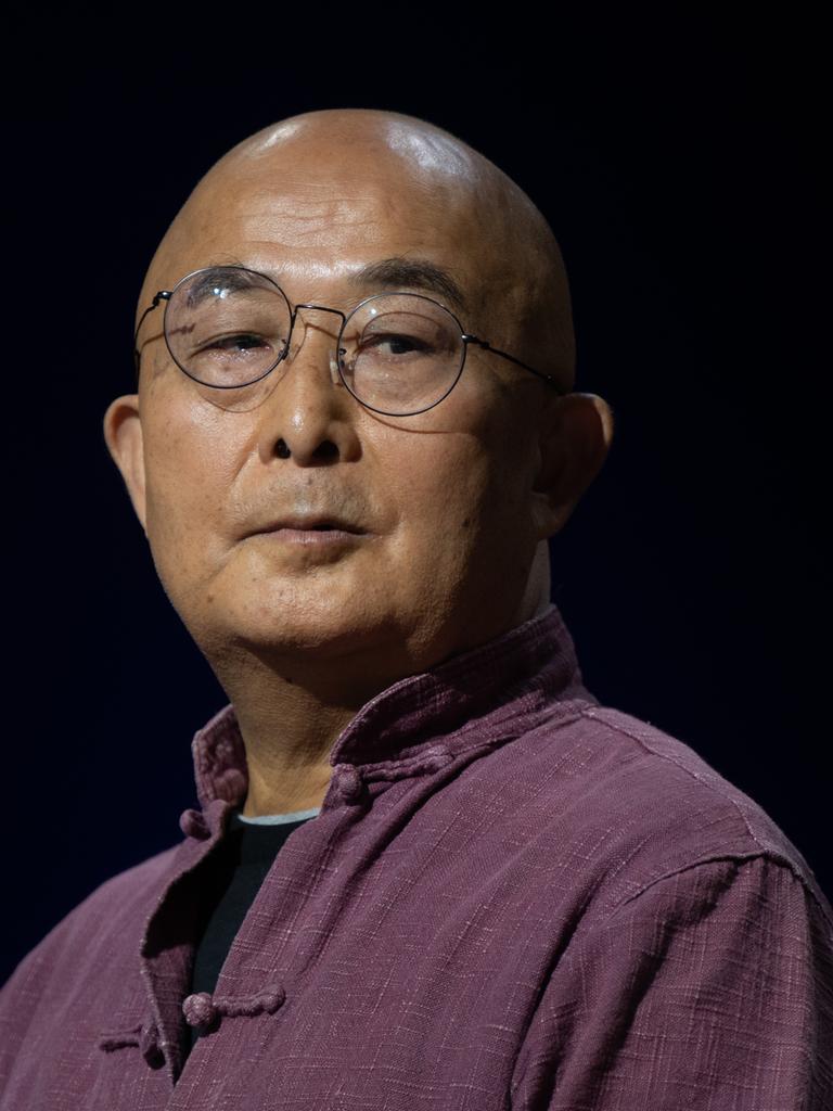 Der chinesische Schriftsteller Liao Yiwu blickt im lila Hemd mit hochgestelltem Kragen, mit Nickelbrille und kahlgeschorenem Kopf über seine Schulter.