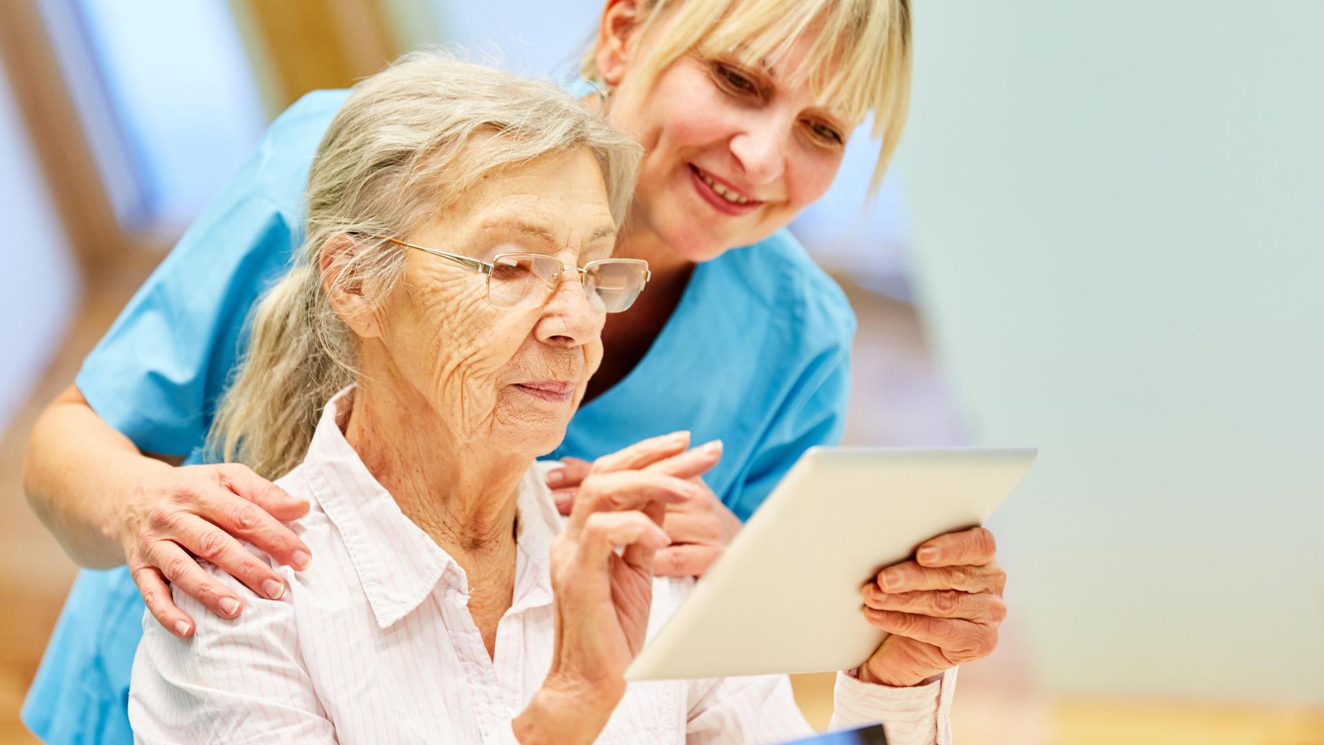 Pflegekraft hilft Seniorin mit Tablet-Computer